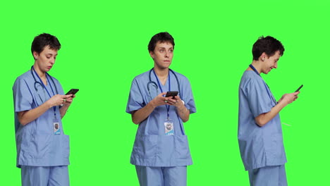 Young-nurse-texting-on-smartphone-against-greenscreen-backdrop